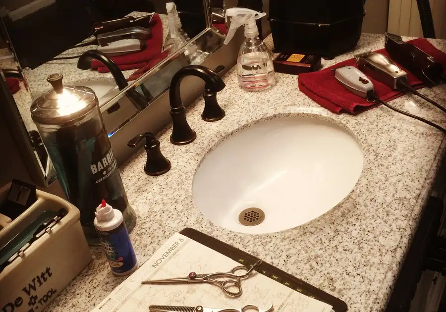 Barber station at GQ Hair Design with clippers on red towels, a Barbicide jar and shears resting on a paper appointment book